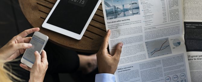 person holding newspaper and tablet on table